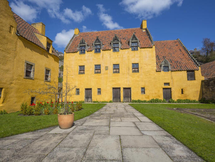 An small, rustic palace painted yellow with red roof tiles and a small lawn on a sunny day.