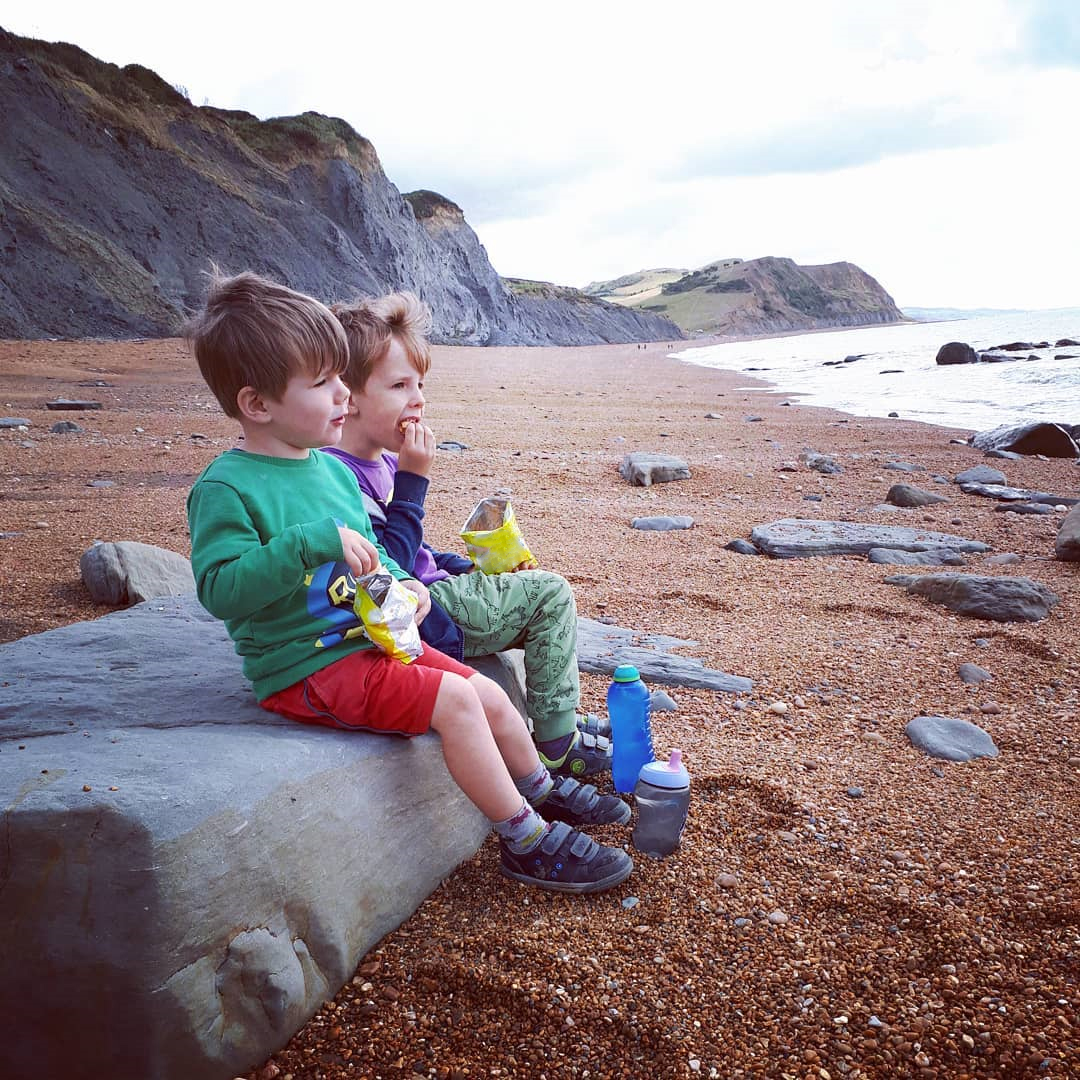 Two boys sitting on a rock and eating crisps on a beach
