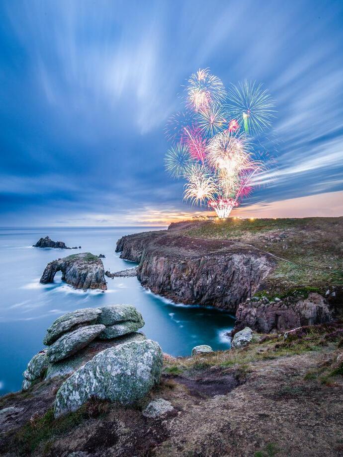 Firework display seen from across a rocky headland at twilight