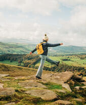 Woman skipping on rocks at edge of hill. Landscape view