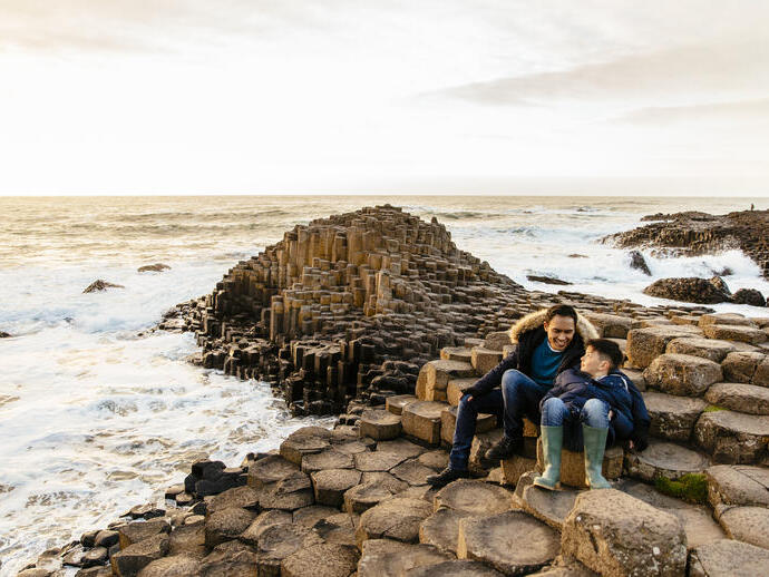 Hombre y niño sentados sobre formaciones rocosas junto al mar