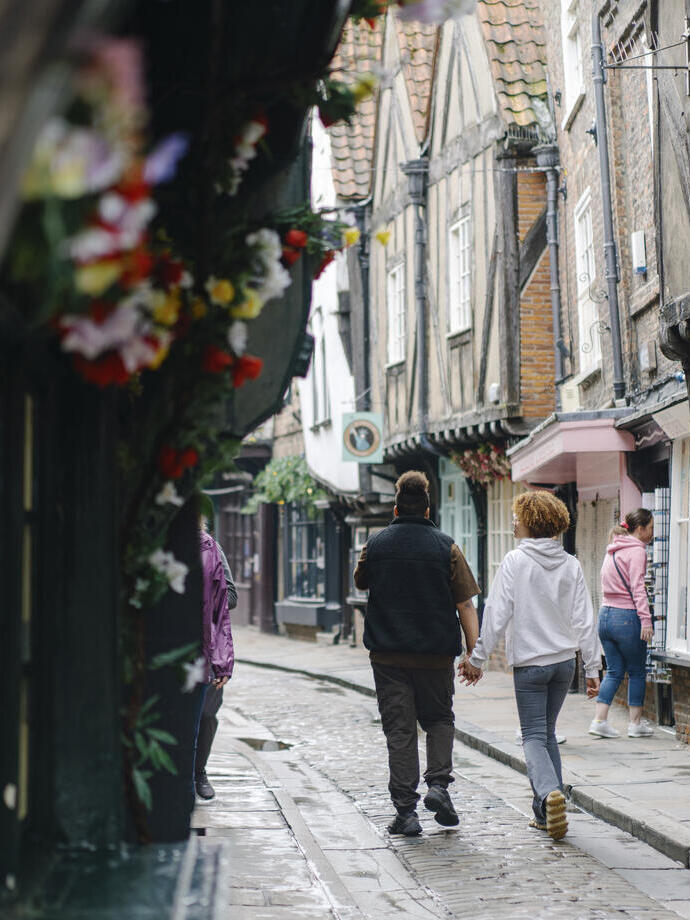 A man and a woman walk down a cobbled street holding hands