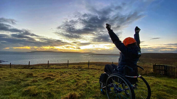 Wheelchair user, arms outstretched looking over the sea, watching the sunrise