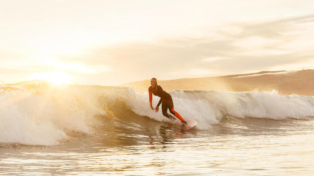 Woman, in black and red wetsuit, surfing a small wave in the sea