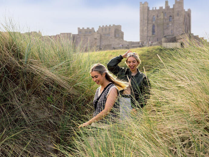 Zwei Frauen spazieren in den Sanddünen am Meer mit einer Burg im Hintergrund