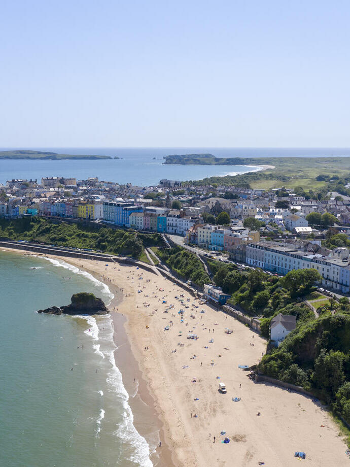 Vue aérienne d'une plage de sable bordée de baigneurs, entourée de maisons de ville aux couleurs vives et de campagne.