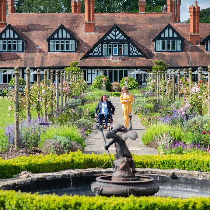 A woman and a man in a wheelchair smiling together in summer gardens