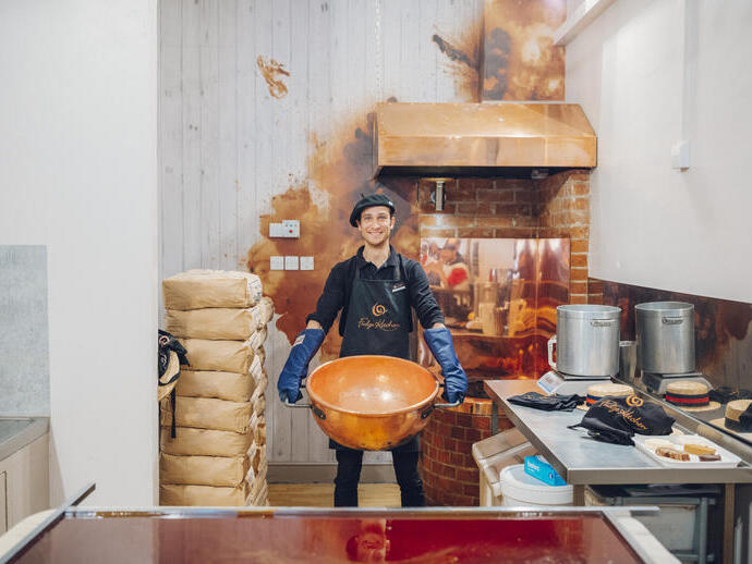 Man in a beret and protective clothing holding a large copper pan