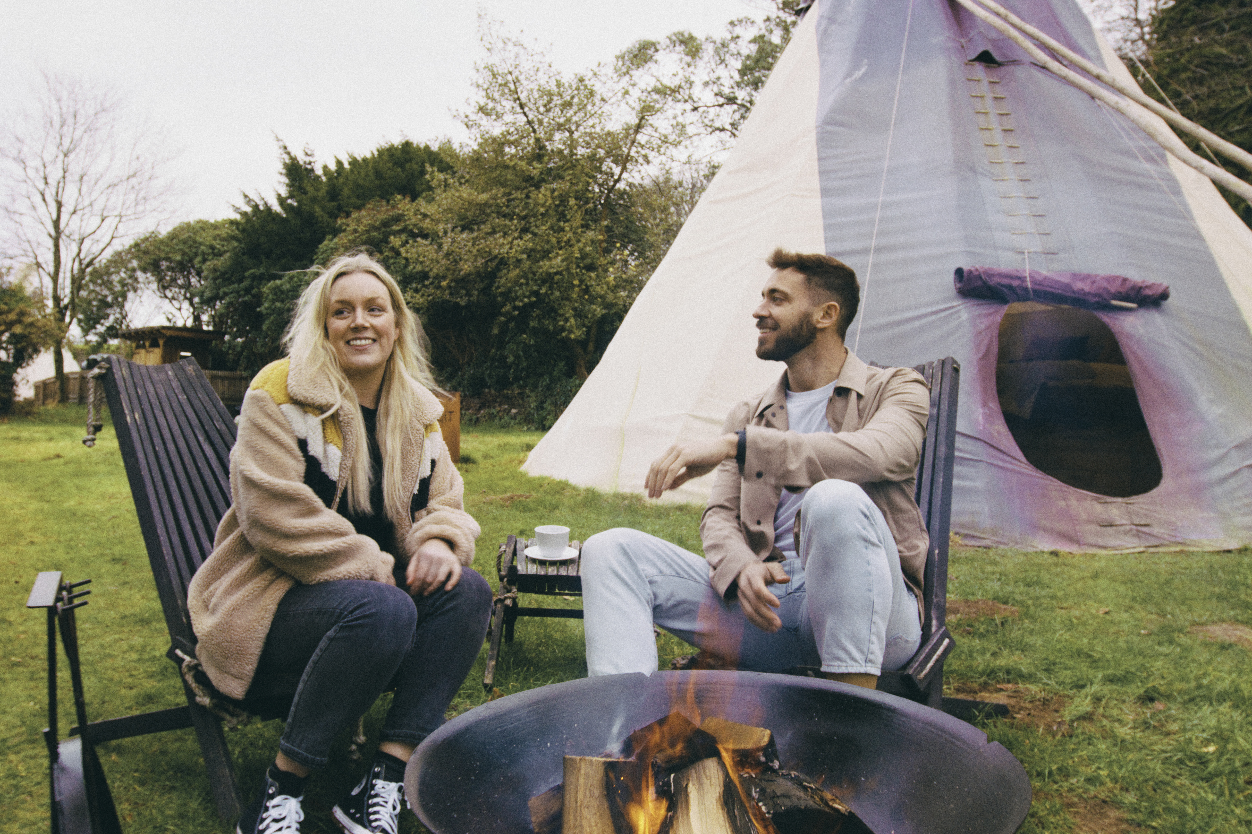 Man and woman sat around a fire, by a tepee