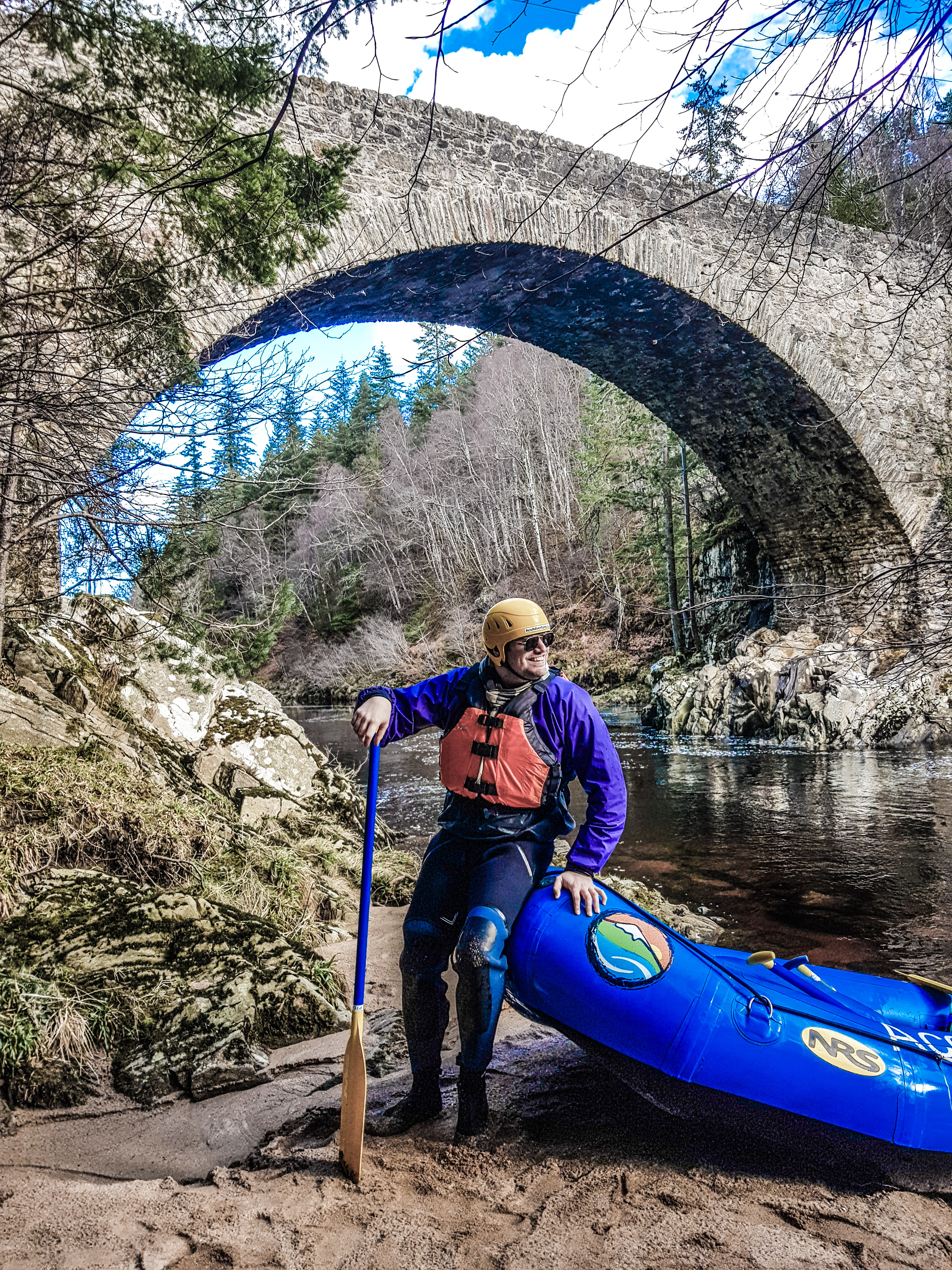 Un homme avec un canoë bleu debout sur les rives d'une rivière près d'un pont