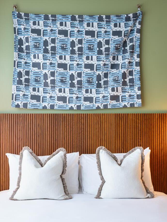 Modern hotel room with a double bed, two white pillows, wooden headboard, wall art, and two round wall lamps on either side of the bed.