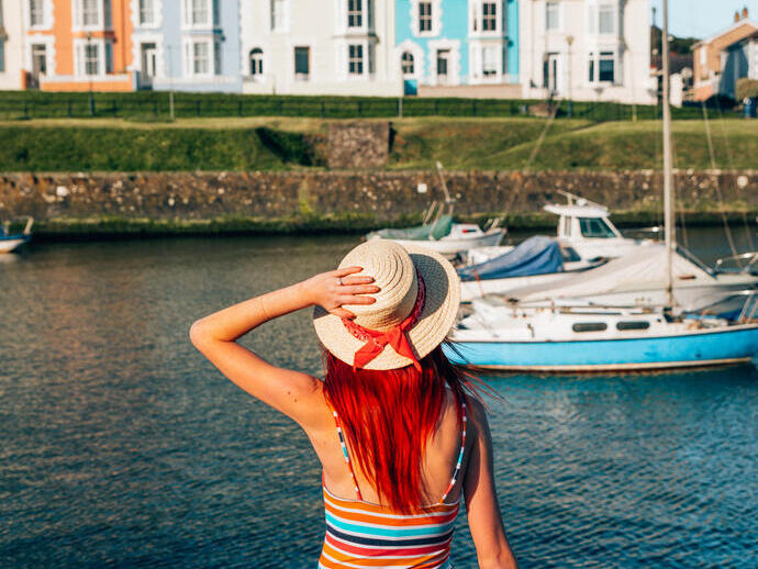 Woman sitting on the wall of a harbour looking at the boats