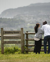 A man and a woman stand at gate with the town and sea beyond