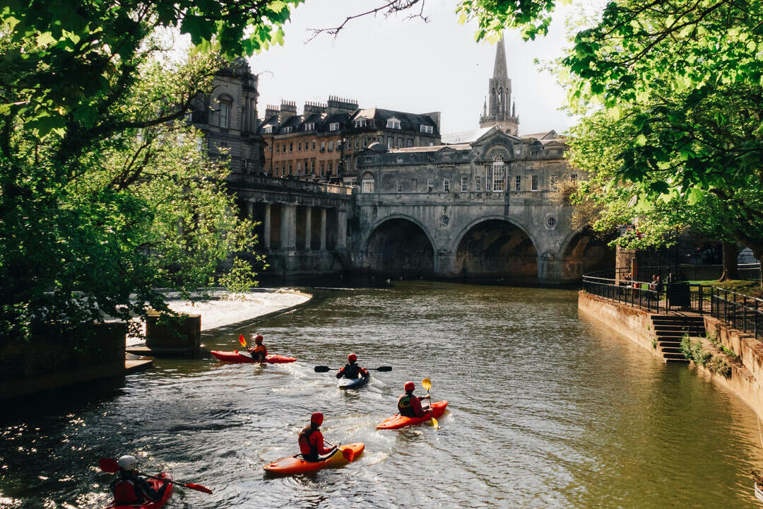 Group of people kayaking on the river by a bridge in a city