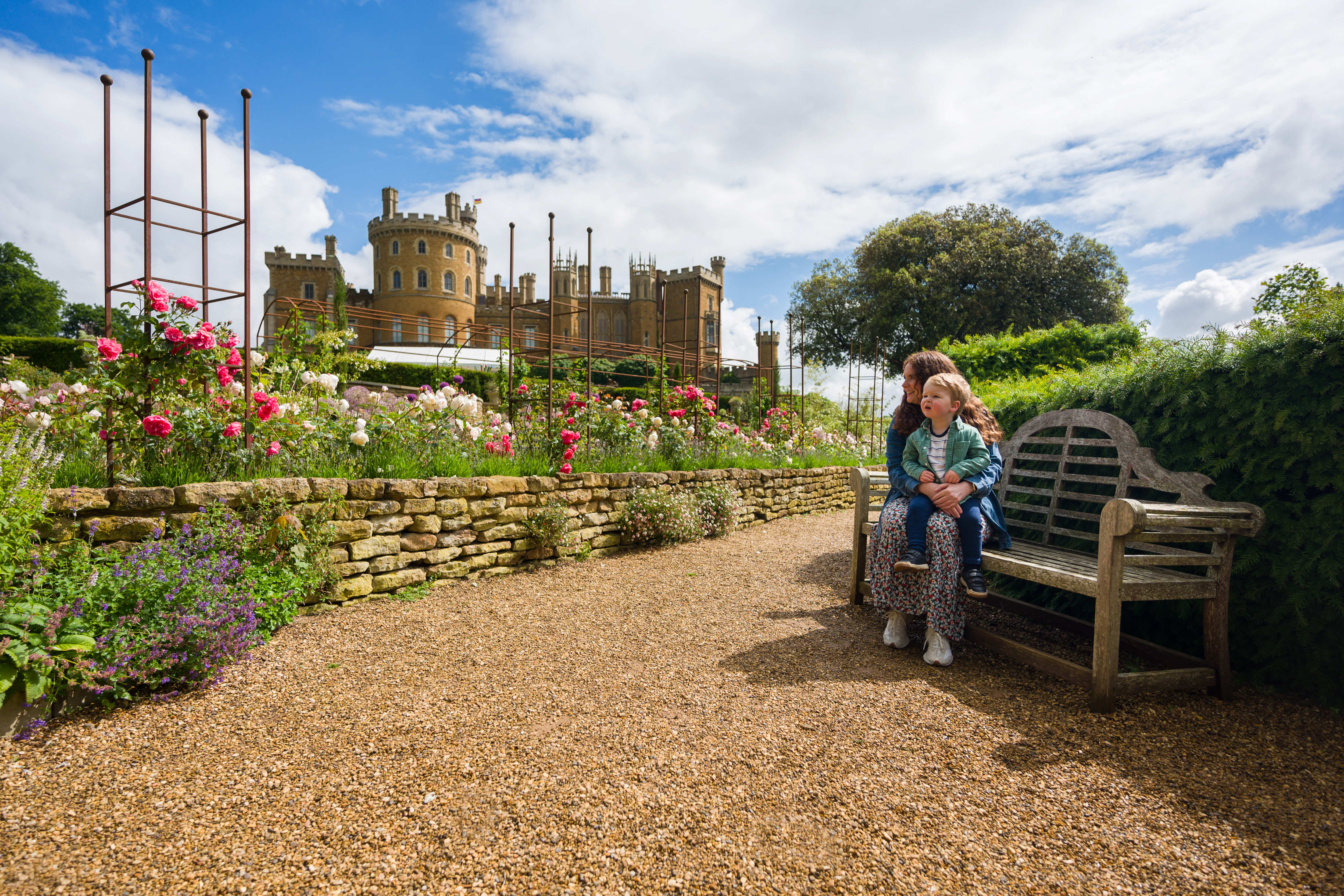 A woman sits on a bench with her child on her lap in front of a castle 