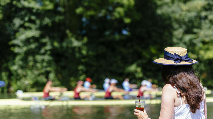 امرأة ترتدي قبعة، تشرب بينما تشاهد سباق قوارب