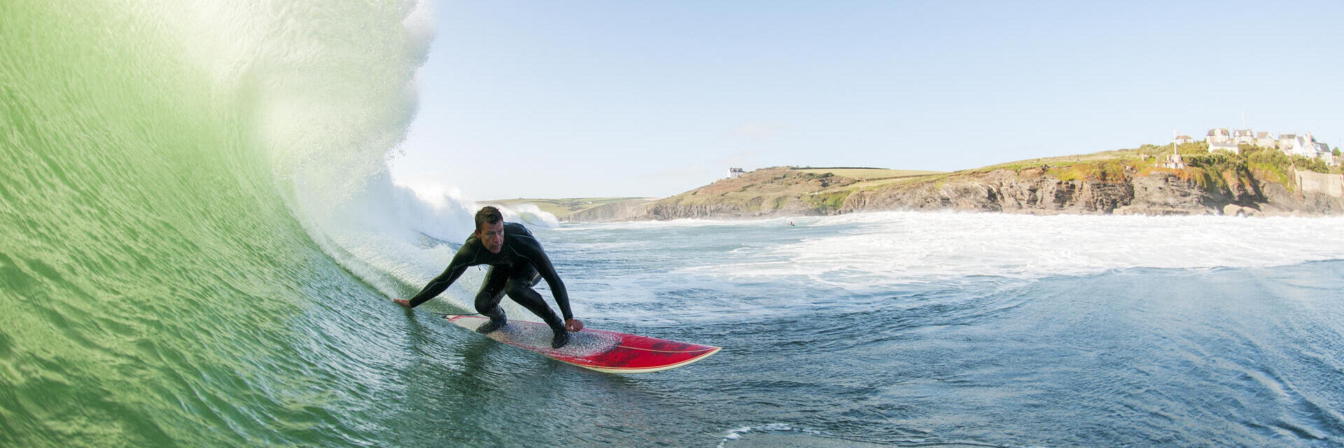 Surfista in muta che cavalca un'onda grande su una tavola da surf rossa in mare