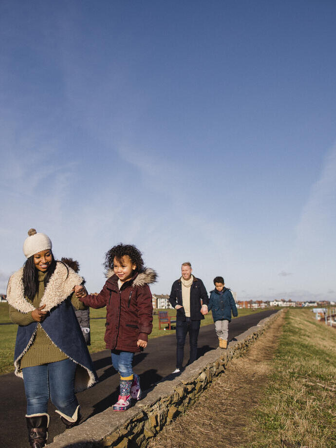 Family and friends walking along a coastal path in the winter sunshine