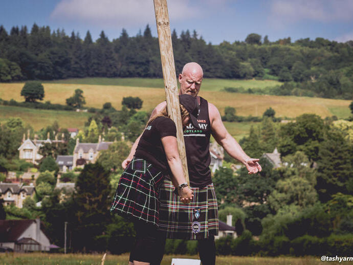 Woman wearing a kilt learning how to toss the caber with male instructor