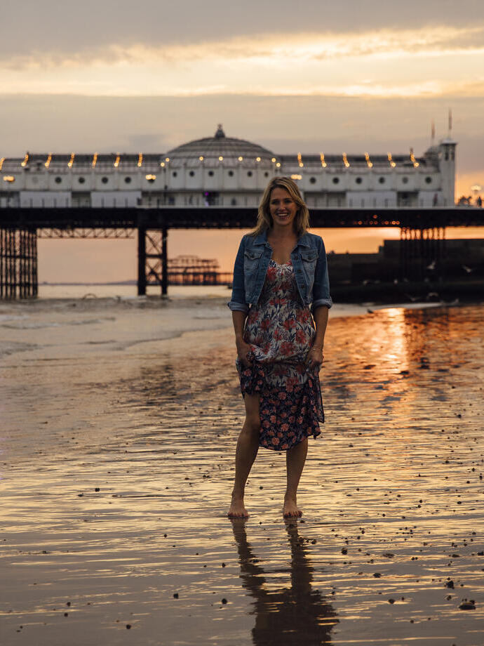 Frau, die bei Sonnenuntergang am Strand in der Nähe des Piers steht