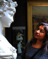 A woman looking at a sculpture on a pedestal in an art gallery