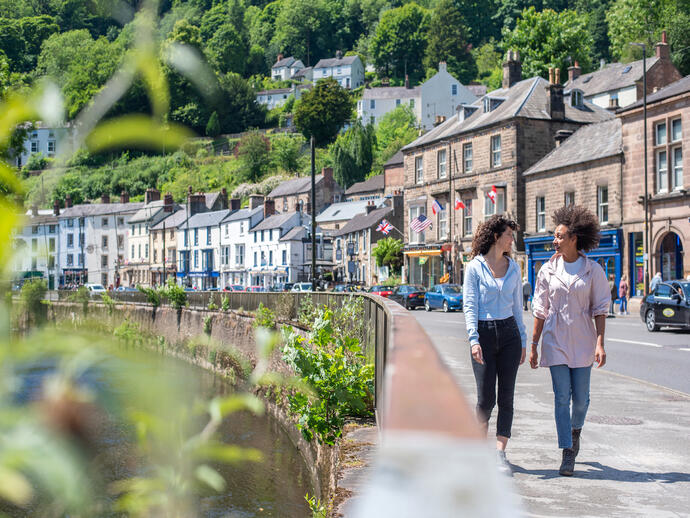 Two women walk down a main street in a hillside town