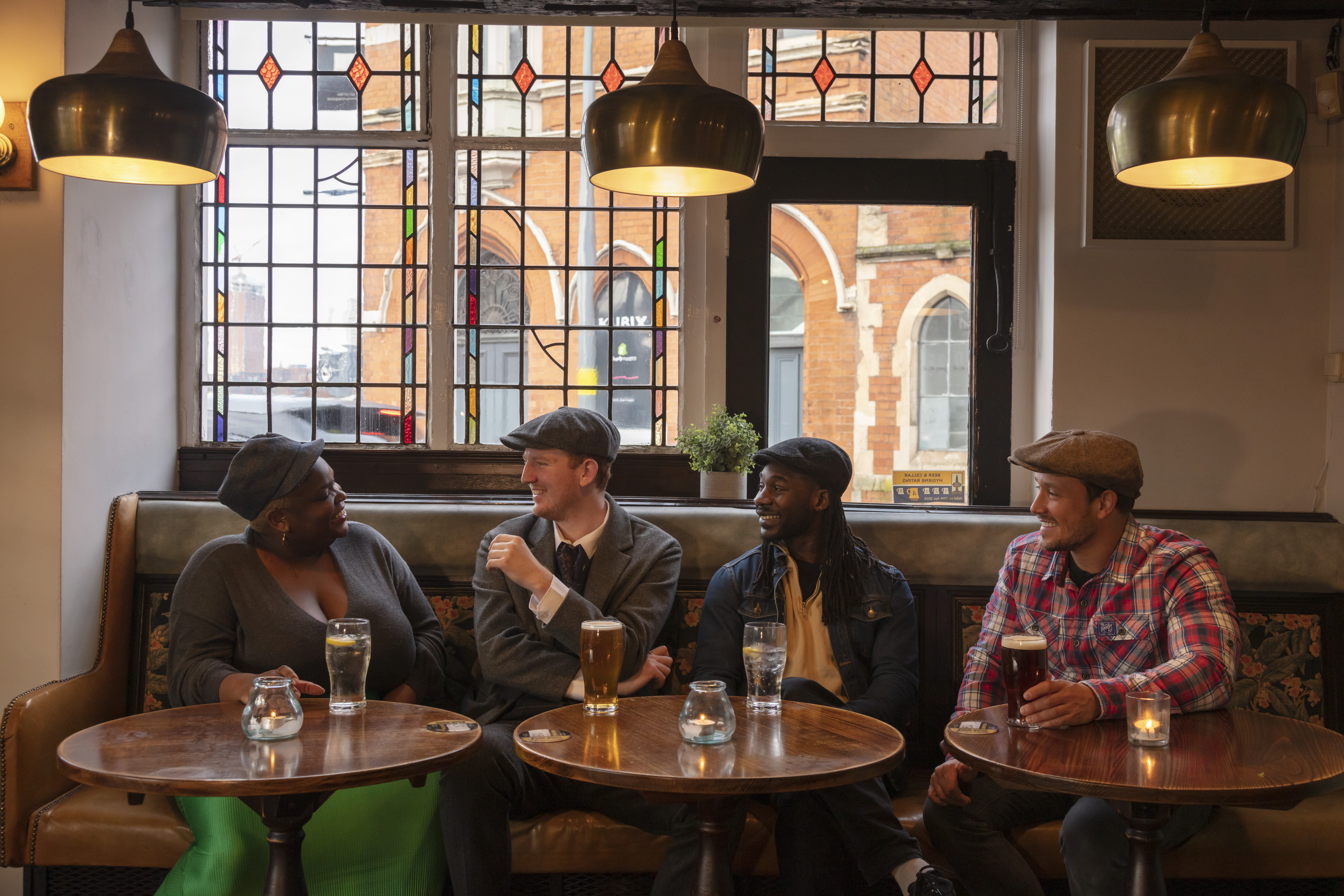 Quatre amis assis à une table près de la fenêtre dans un pub en train de boire un verre