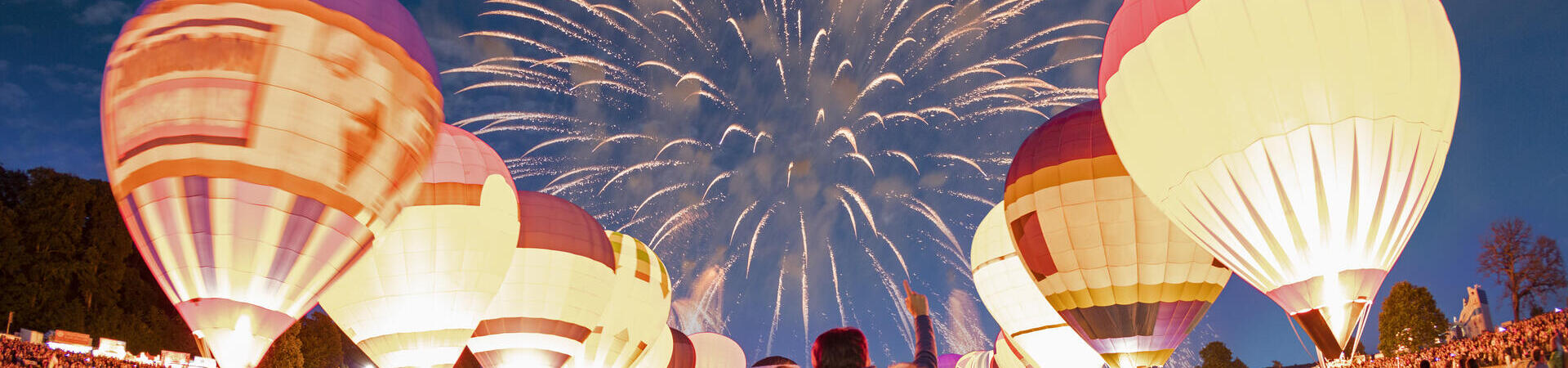 Couple watching grounded hot air balloons and fireworks in the night sky