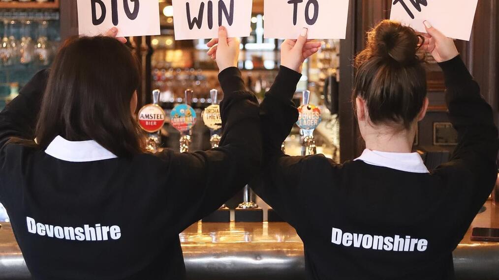 Two female staff from Devonshire Balham Public House holding signs for free tickets to Six Nations Rugby