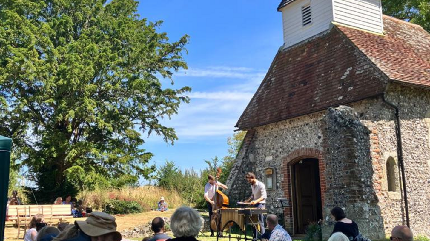 Grupo de personas viendo un concierto al aire libre junto a la iglesia en el Festival Microconcert