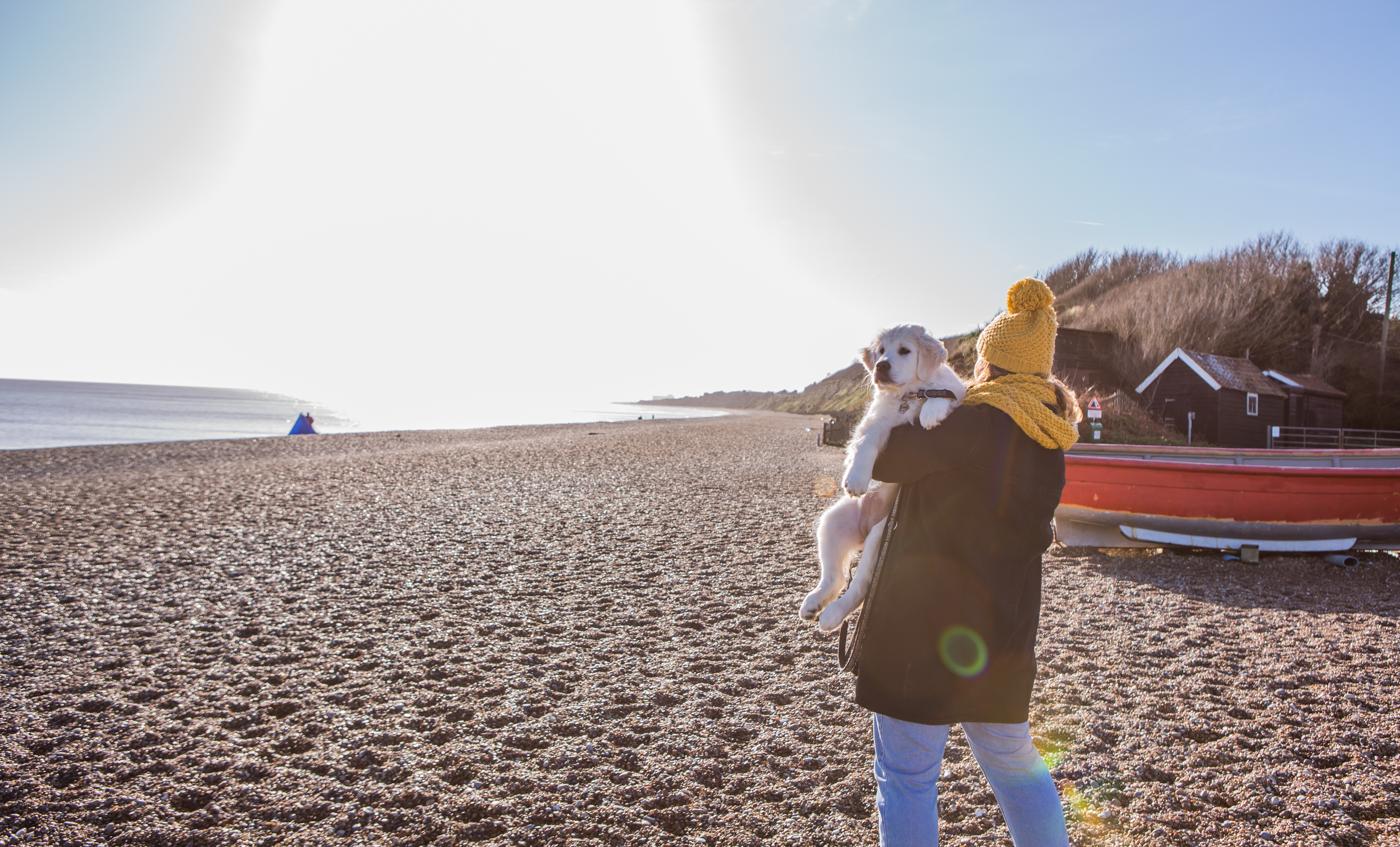 A woman carrying a dog along a beach in Dunwich