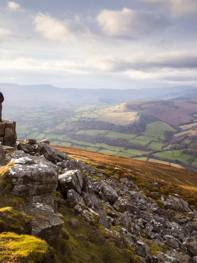 Uomo in cima a una vasta catena montuosa colorata al tramonto che guarda verso la valle