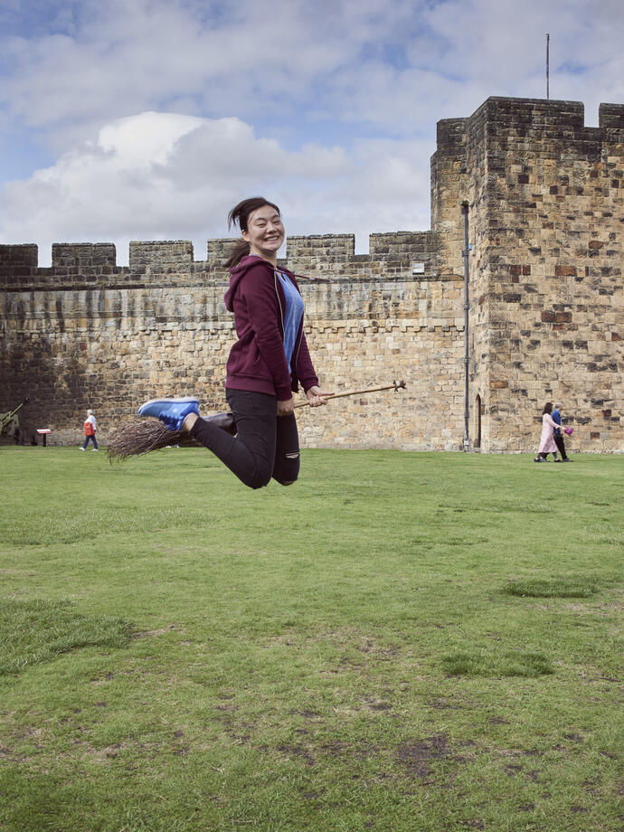 Young woman hovering on a broomstick in the Outer Bailey of Alnwick Castle