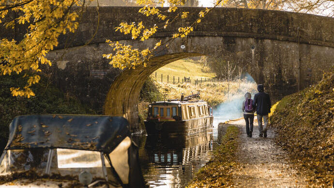 Man and woman walking beside a canal near a low bridge