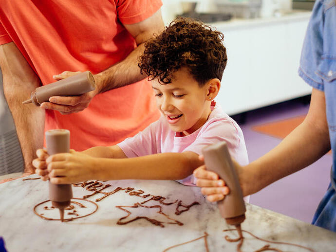 Un ragazzo con i capelli ricci che spreme il cioccolato da una bottiglia