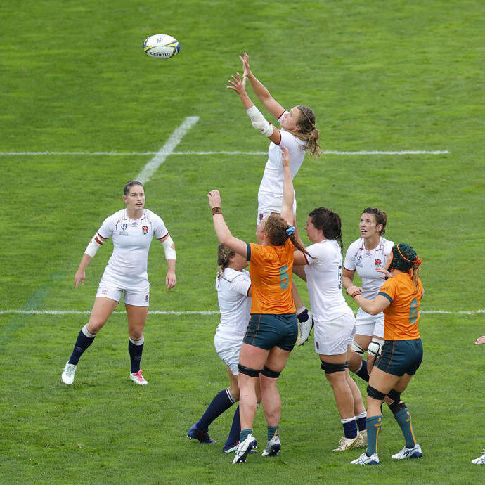 Women's rugby match with players from two teams jumping to catch the ball on the field