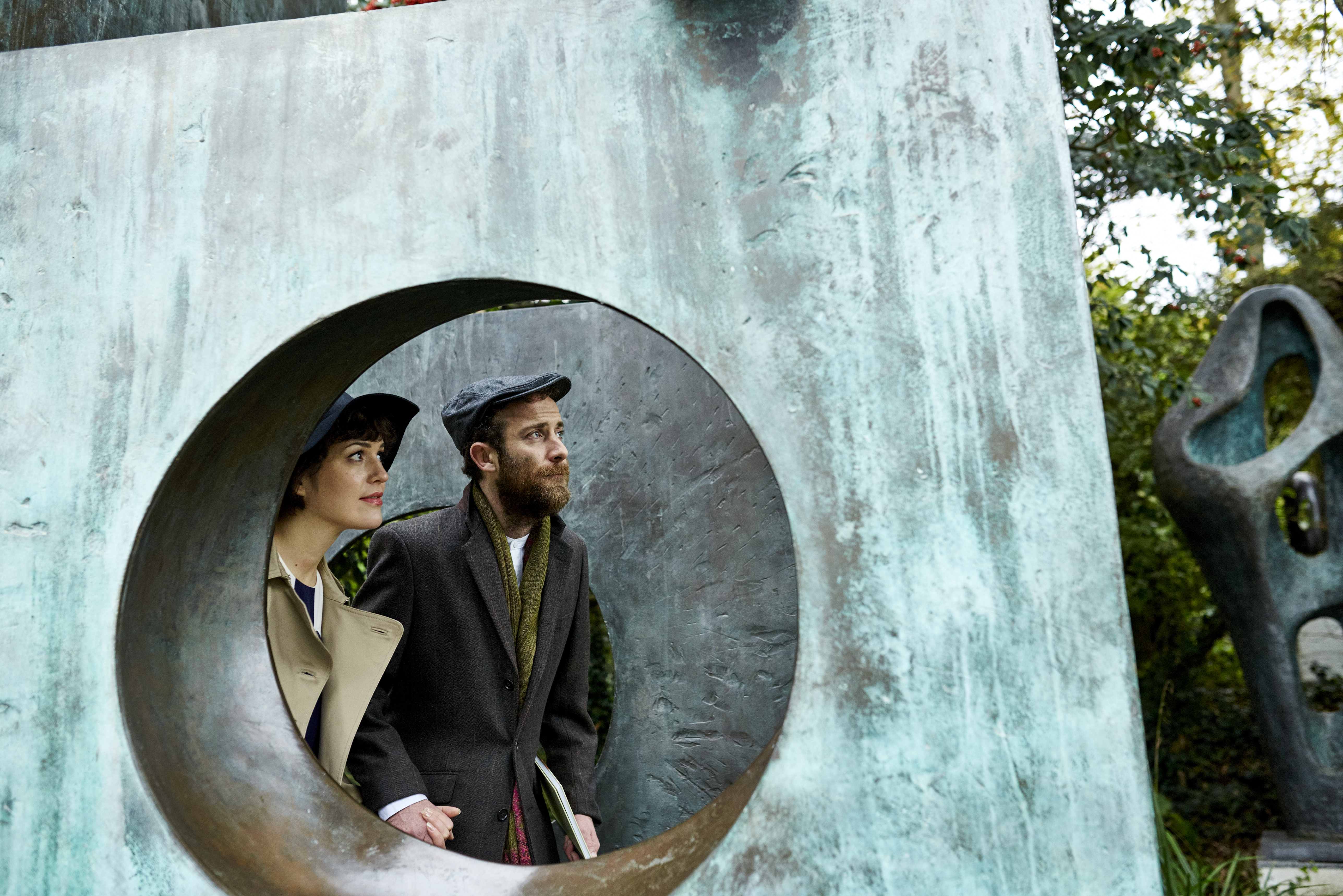Couple seen through a gap in a large bronze sculpture in a garden