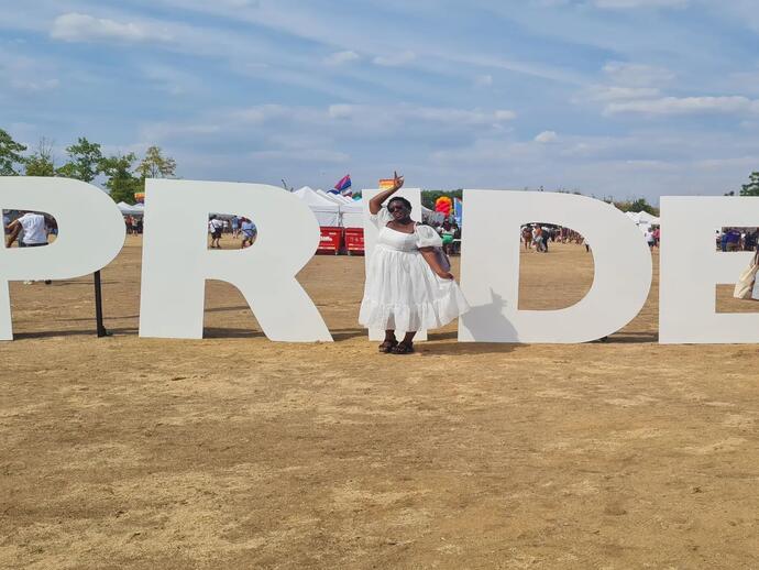 Woman in white dress standing in front of UK Black Pride sign