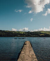 Un muelle que se adentra en un lago en el Parque Nacional de Snowdonia/Eryri con barcos pasando en la distancia