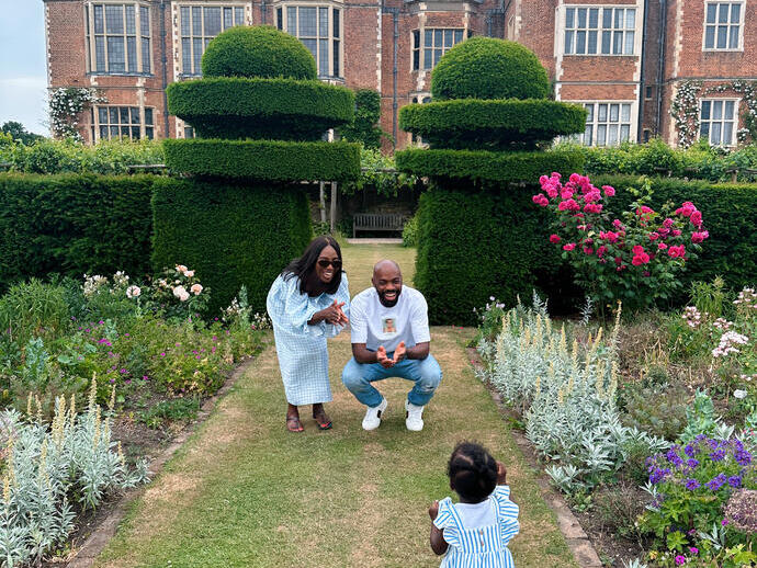 Man, woman and child playing in formal garden of large country house