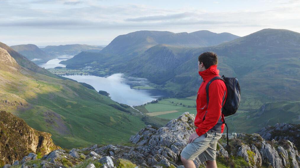 رجل يحمل حقيبة ظهر يقف على قمة جبل يطل على التلال والبحيرة