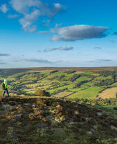Eine Frau spaziert einen Pfad entlang auf einem Hügel und genießt die Aussicht.