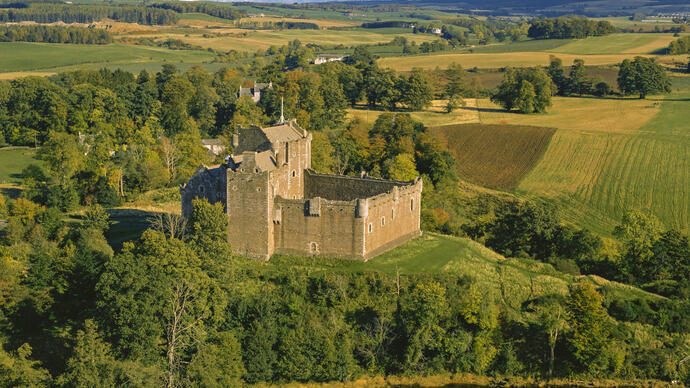 Extérieur d'un château médiéval en partie en ruines sur une petite colline surplombant des champs et des arbres en automne.