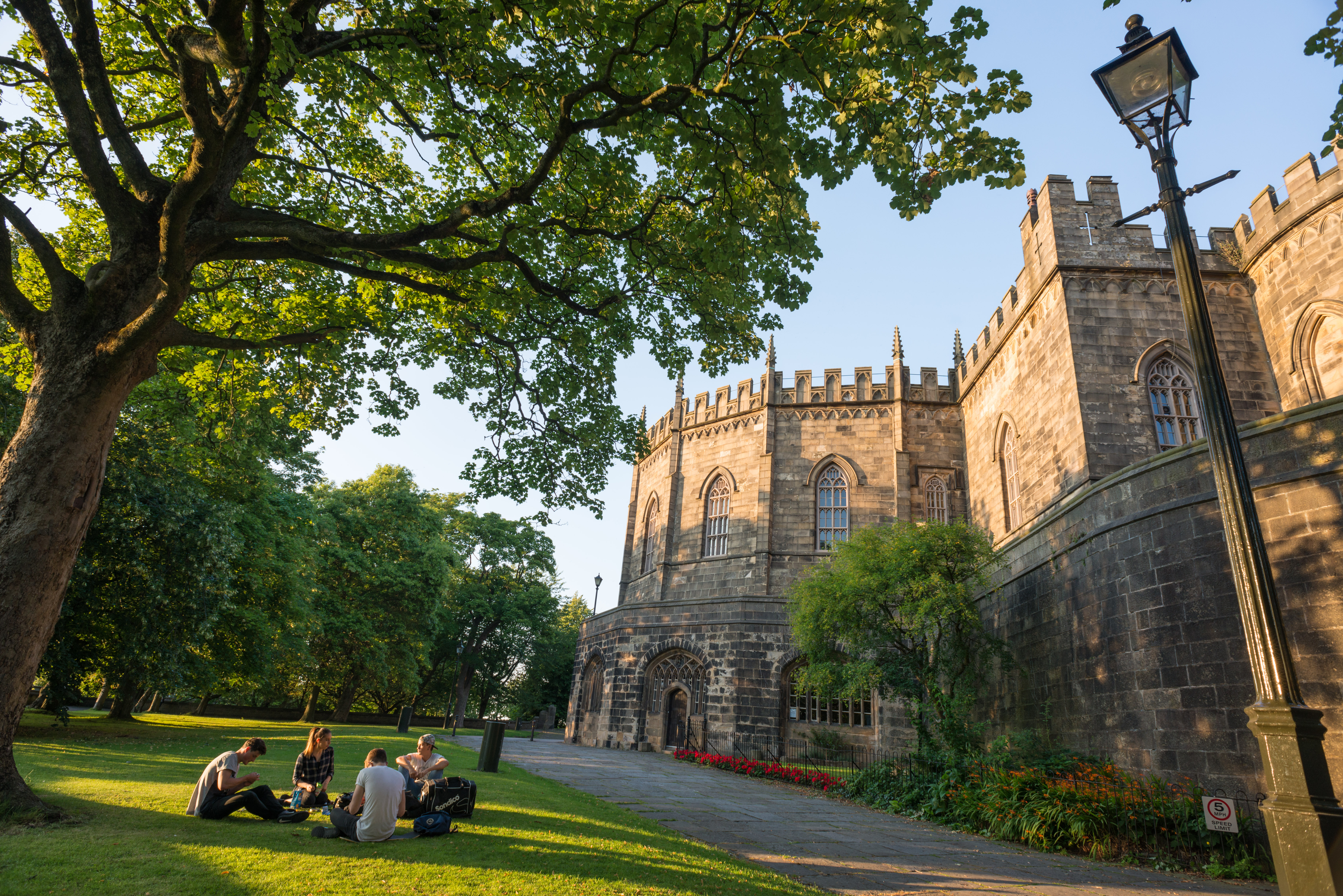 External view of Lancaster castle with visitors sitting around the lawn in the foreground
