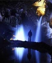 Homme debout à côté d'une cascade dans une grotte sombre