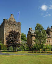 Esterno di un piccolo castello con un pennone e alcuni alberi in una giornata di sole.