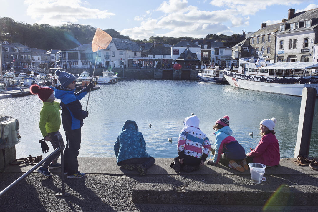 Children sat on a harbour wall fishing for crabs