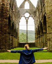 A woman with arms out stretched inside a vacant crumbling church