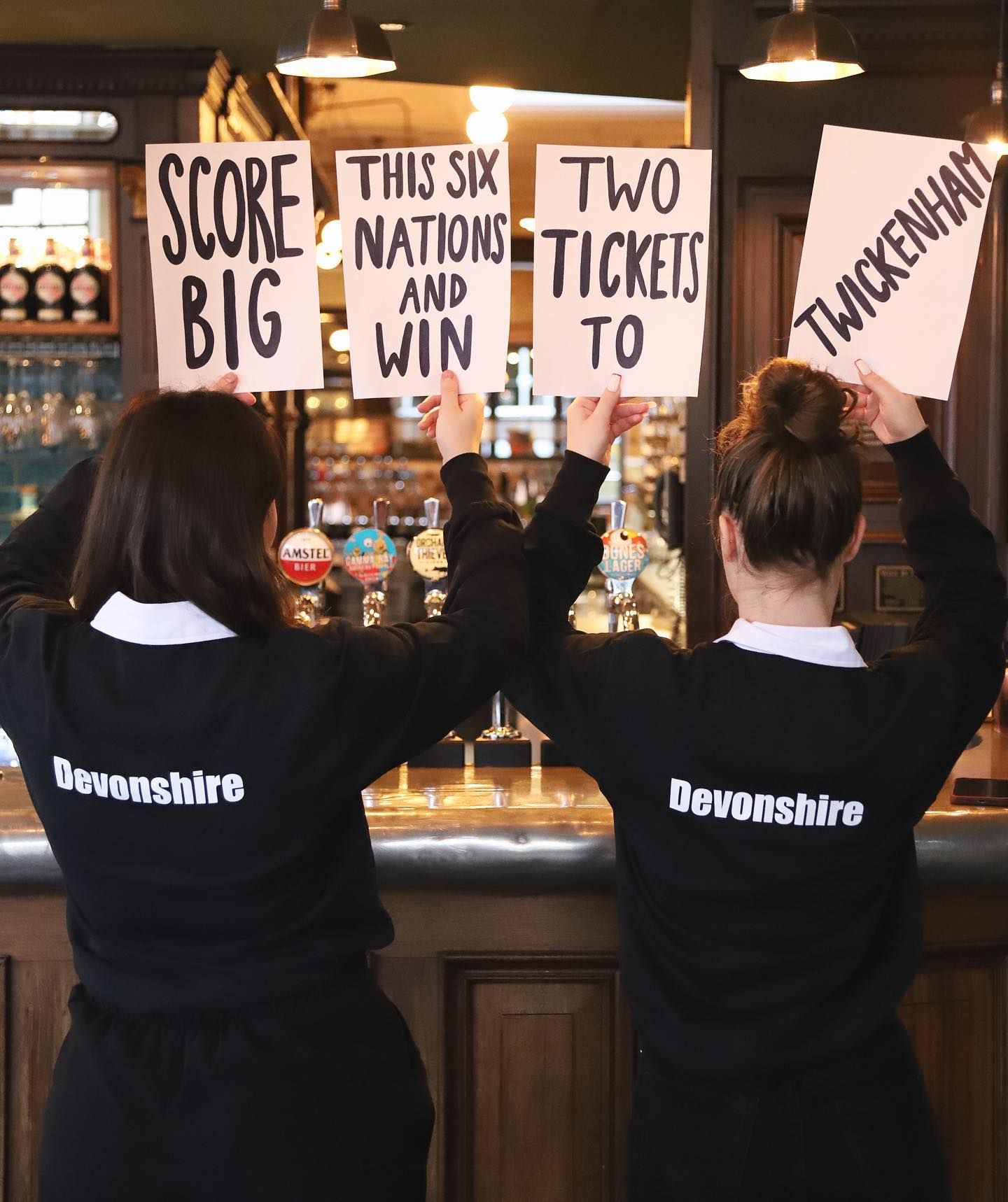 Two female staff from Devonshire Balham Public House holding signs for free tickets to Six Nations Rugby, Twickenham