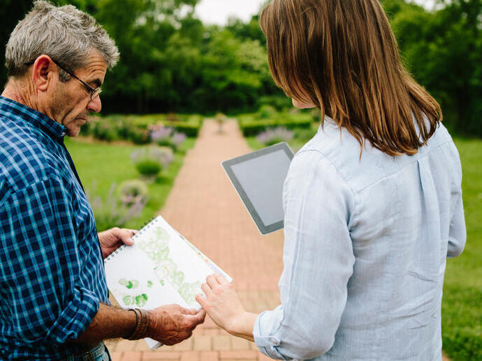 Man and woman sharing garden plans and designs stood on a path in a garden